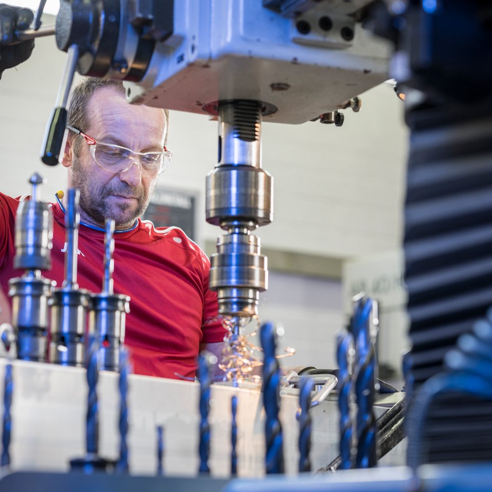 Aluminium bohren Ein Mann bedient einen Bohrer, der Aluminium bearbeitet, Späne fliegen, in Vordergrund mehre Bohrköpfe.